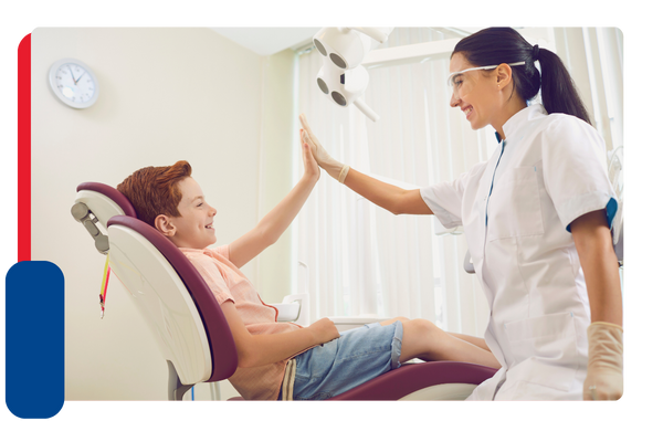 A young boy smiles and high fives a hygienist while sitting in a dental chair