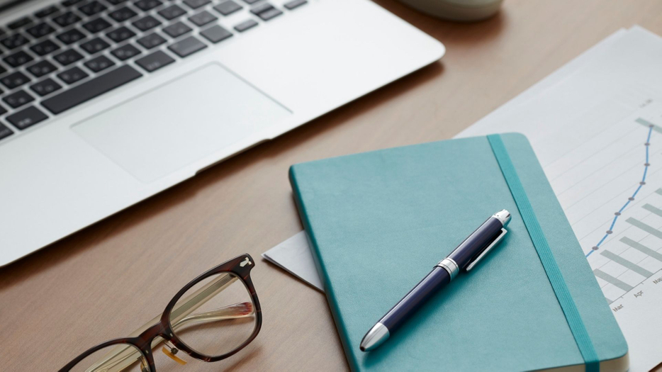 glasses and notebook on a desk with laptop