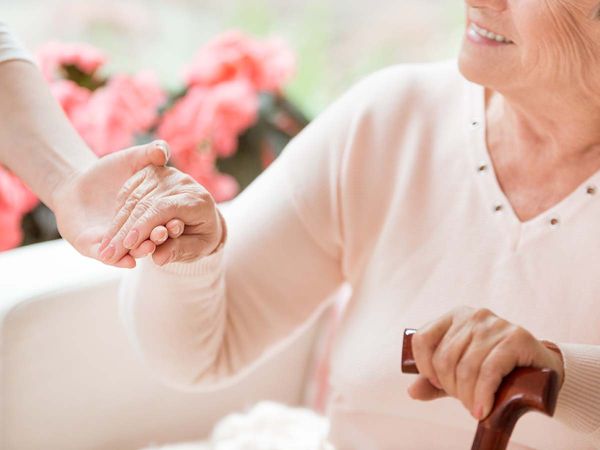 Close-up of caregiver supporting smiling senior women with walking stick