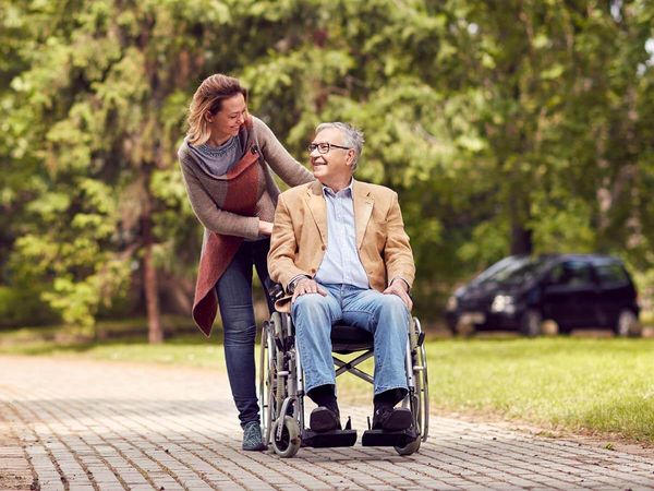 Caring woman and senior man in wheelchair on walking green nature