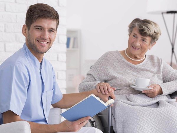 Nice male caregiver and senior woman on a wheelchair holding his hand