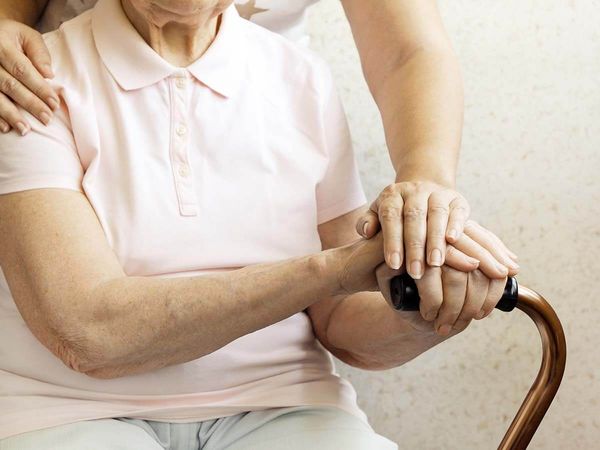 Senior woman holding quad cane handle in elderly care facility.