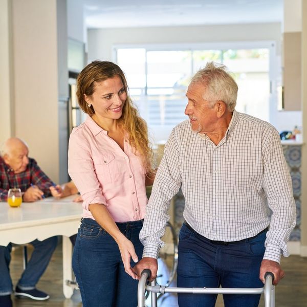 An image of a young woman helping an old man with a walker.