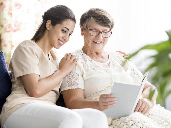 Senior women and a young nurse reading a book together in a nursing home