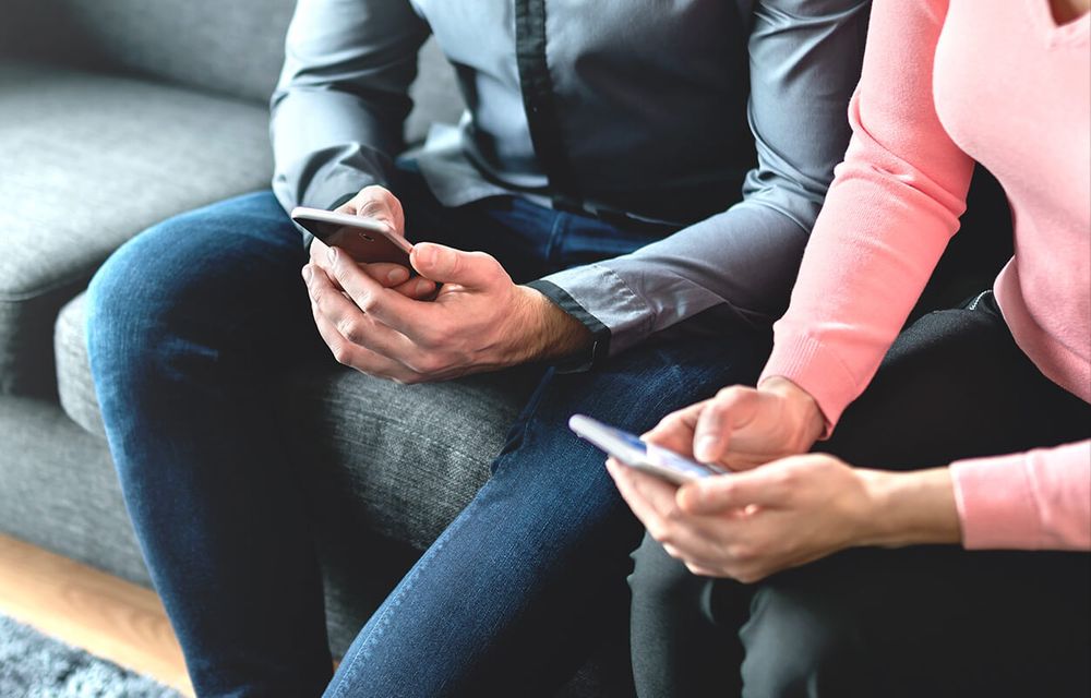 2 people sitting on couch looking at phones