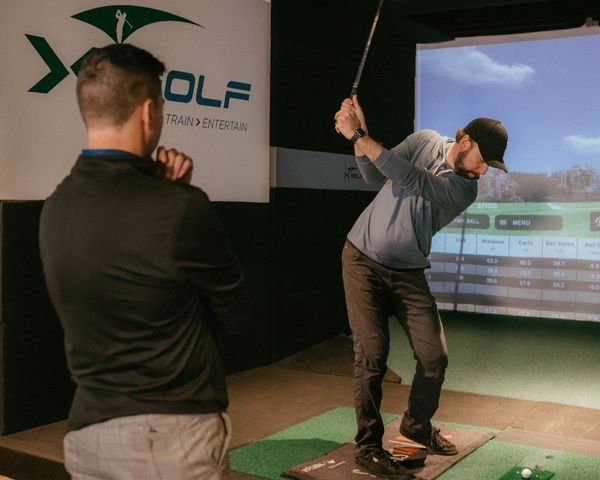 man practicing swing at X Golf while instructor watches