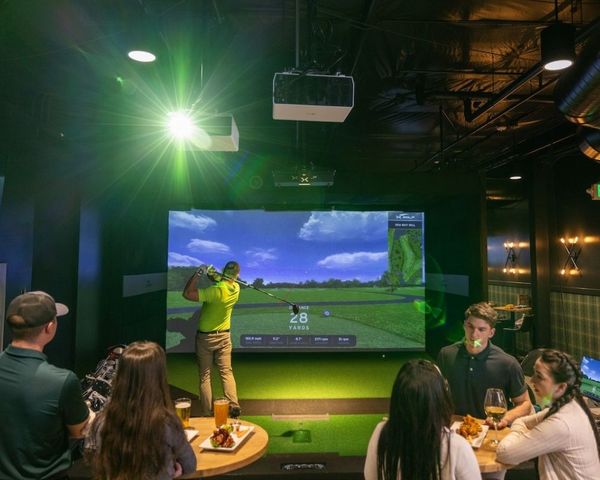 golfer practicing drive at X-Golf with group of friends watching