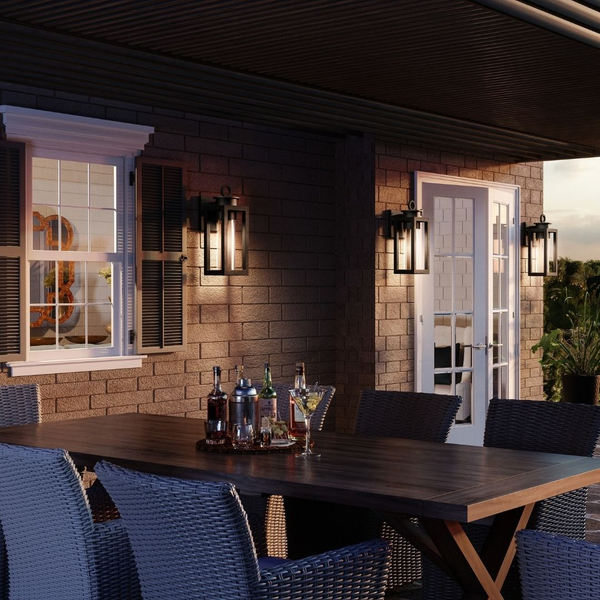 Black rectangular wall sconces mounted on a brick patio wall above an outdoor dining setup.   