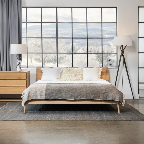 light bedroom with a table lamp and a floor lap with a large window behind the bed