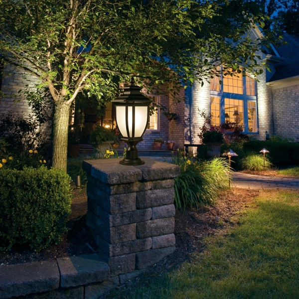 Traditional black post lantern mounted on a stone pillar illuminating a front lawn and tree.   