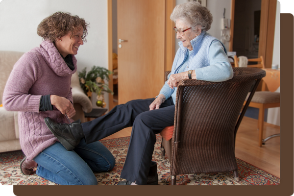 older woman sitting in a chair getting help putting on her shoes