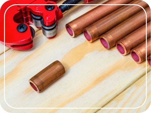 Red pipe cutter and copper pipes with connectors for plumbing repairs.