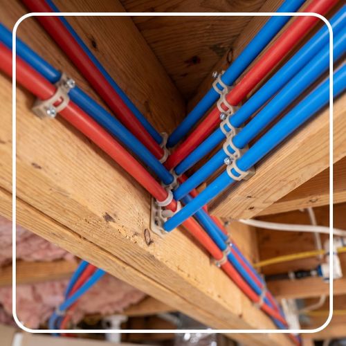 Flexible red and blue PEX tubing neatly secured to a wooden beam.