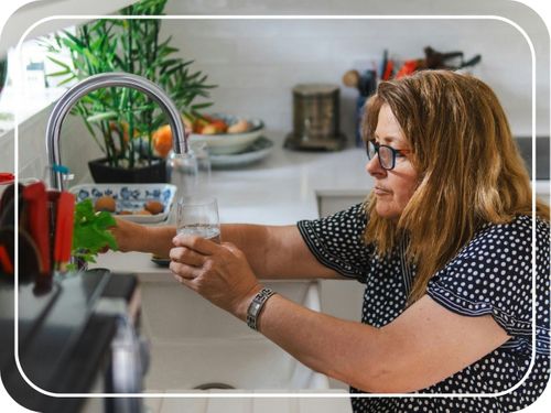 woman fills glass of clean water from kitchen sink 