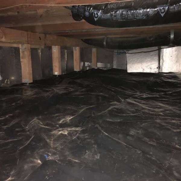 A dark crawl space with a black vapor barrier laid across the ground and insulation visible above.