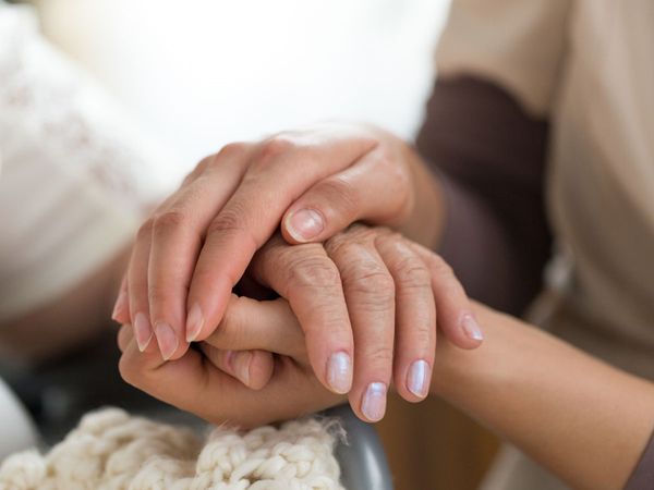 An image of a woman holding an elderly woman’s hand.