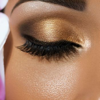 Closeup of eyelid with gold eyeshadow, liner, and eyelash extensions