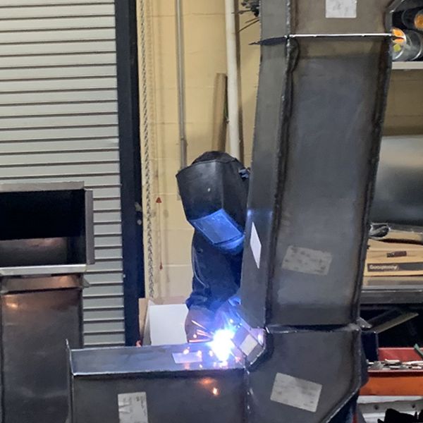 Person welding duct work pieces together.