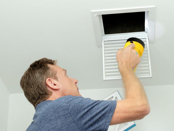 Man inspecting air ducts, shining a flashlight through a small square ceiling vent. Man inspecting air ducts, shining a flashlight through a small square ceiling vent.