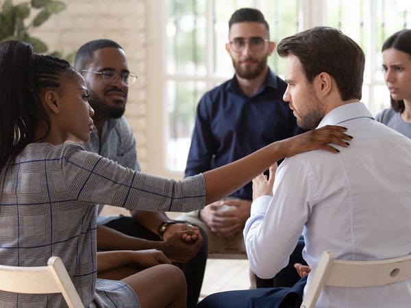 People of support group sitting in a circle together, with one female participant gently reassuring a male participant. 