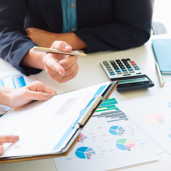Hands analyzing financial charts and documents with a calculator, discussing accounting data.