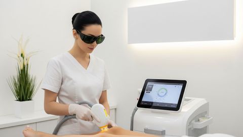 A professional in a clean, modern salon setting operates an advanced laser treatment device.