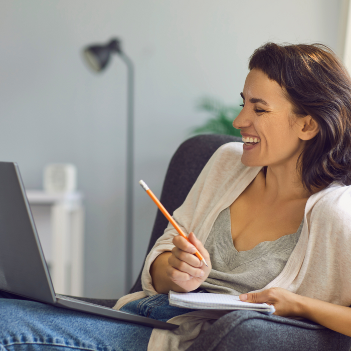 woman holding pencil and paper smiling at laptop