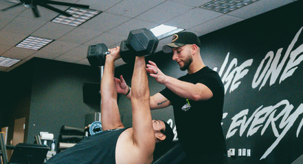 personal trainer helping a man lift two dumbbells.