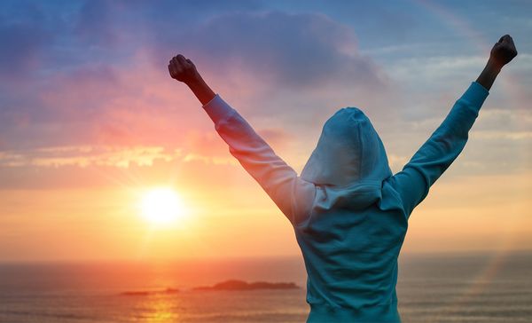 a person raising their hands in the air at the setting sun