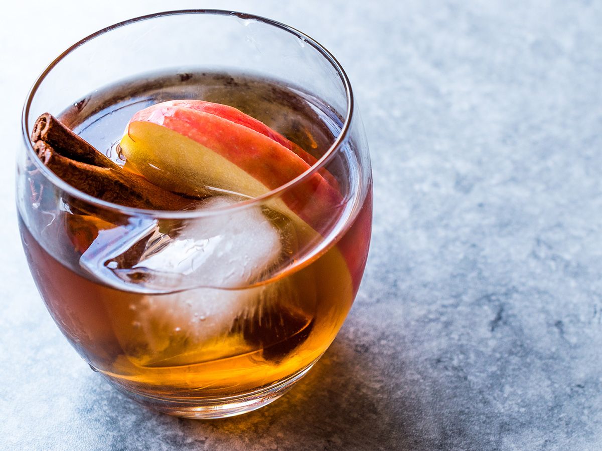 Glass of bourbon garnished with apple slices, ice, and cinnamon sticks.