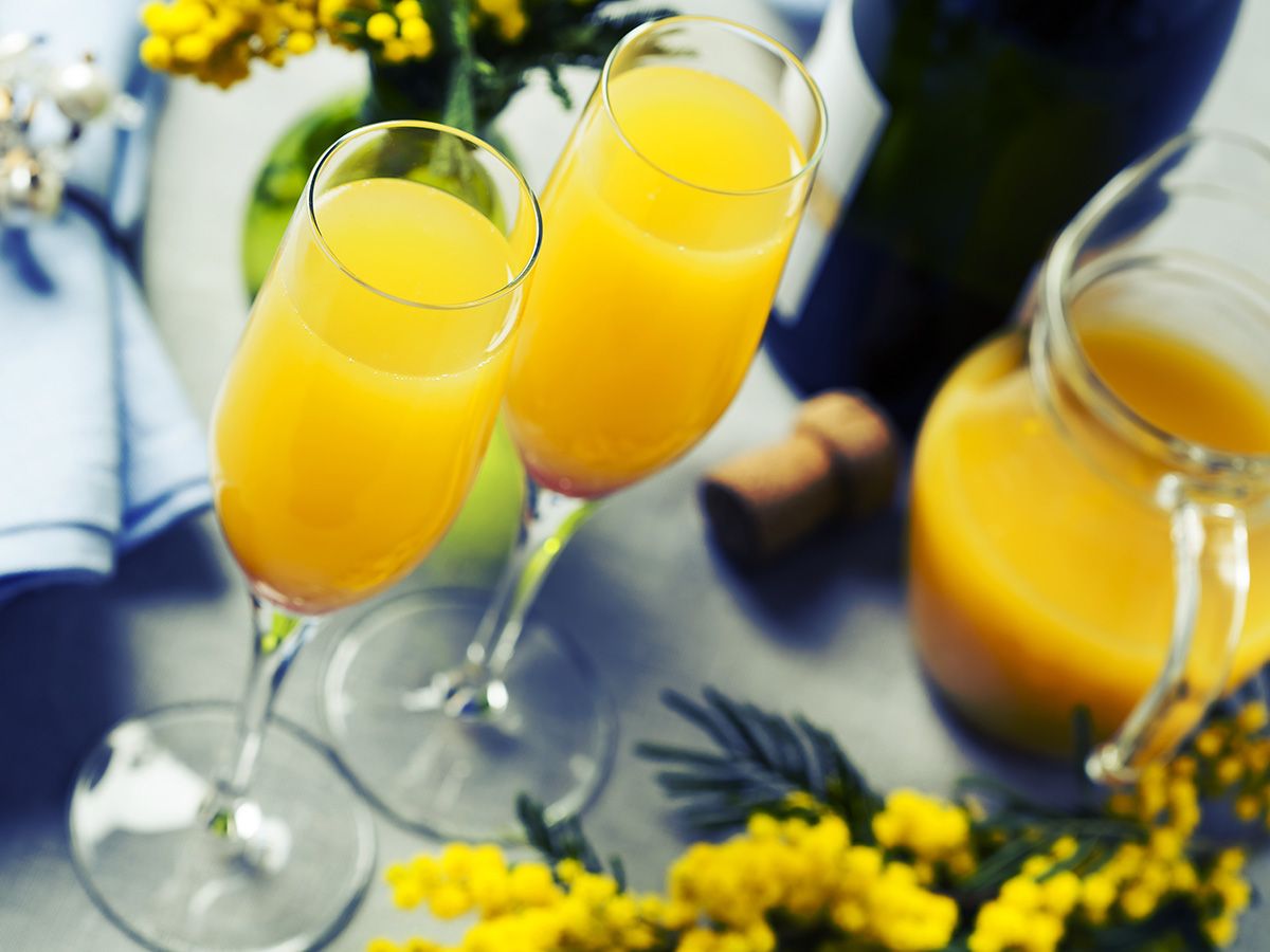 Two mimosas sitting on a table with yellow garnishings behind them. 