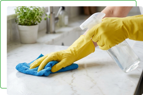 Gloved hands using a microfiber cloth to meticulously clean a white marble kitchen counter.
