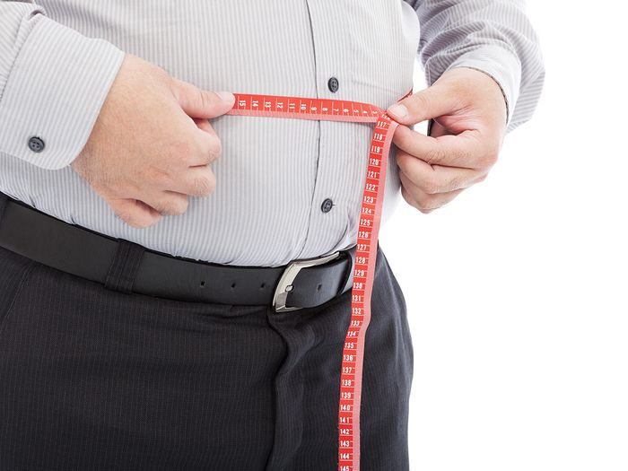 overweight man measuring waistline