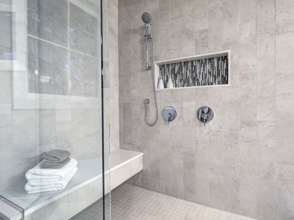 Modern walk-in shower with gray vertical subway tile, glass enclosure, built-in white bench, and recessed storage niche. Modern walk-in shower with gray vertical subway tile, glass enclosure, built-in white bench, and recessed storage niche.