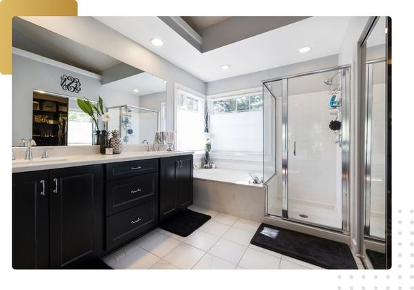 Luxurious master bathroom remodel with dark wood cabinets, dual mirrors, and a glass-enclosed shower/tub area.