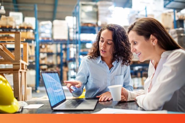 two women in warehouse looking at inventory on laptop