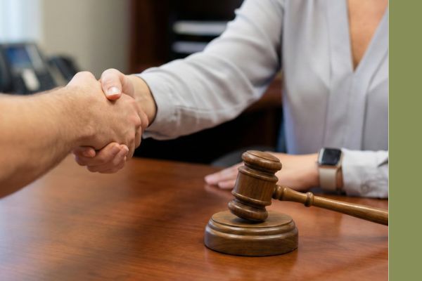 Close-up of a professional handshake between an attorney and a client over a wooden desk with a legal gavel in the foreground.