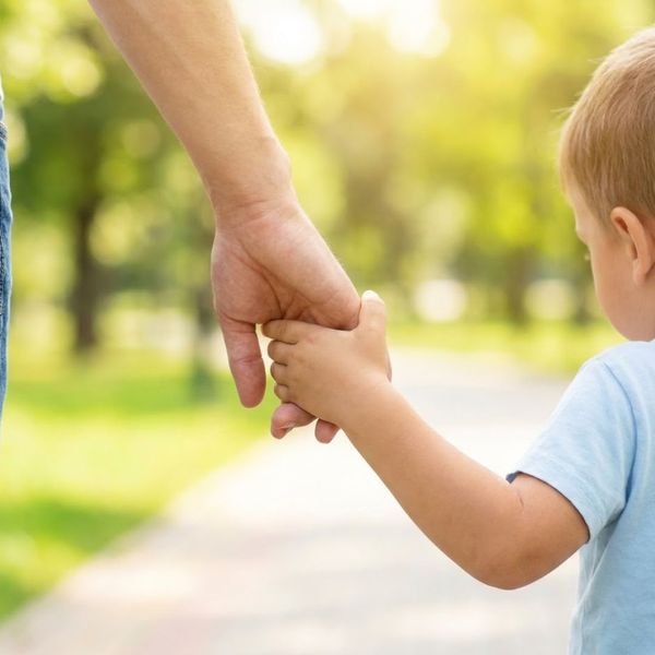 An adult holding a child's hand while walking outdoors, representing child custody