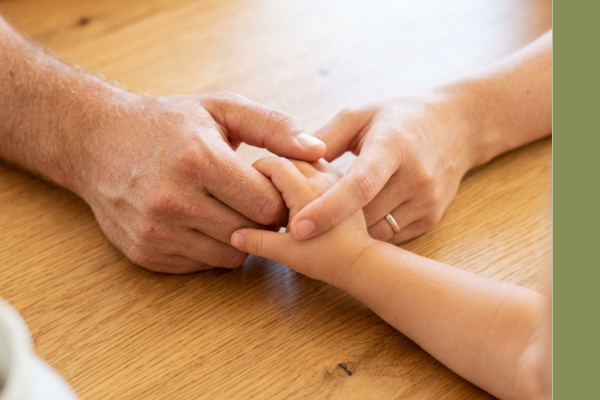 Adults holding a child's hand in a protective and caring gesture.