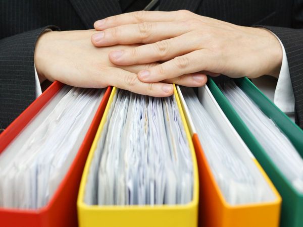 An image of folded hands over binders of paper.