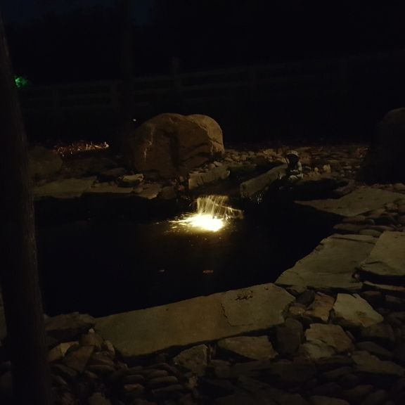 Underwater landscape light illuminating falling water in a koi pond at night