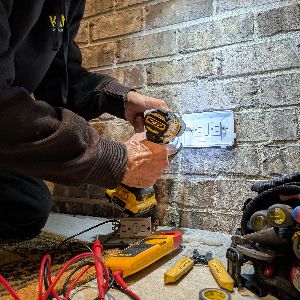 Emergency electrician performing an after-hours GFCI outlet repair on a residential porch with diagnostic tools and replacement materials prepared to restore power safely. Emergency Electrician Performing After-Hours Electrical Repair