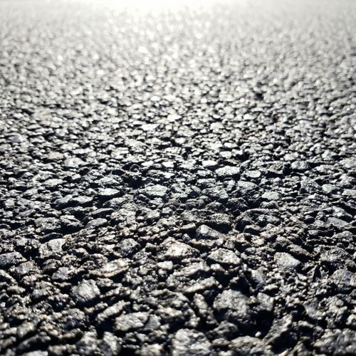 A detailed macro photograph shows the coarse texture of dark asphalt aggregate.