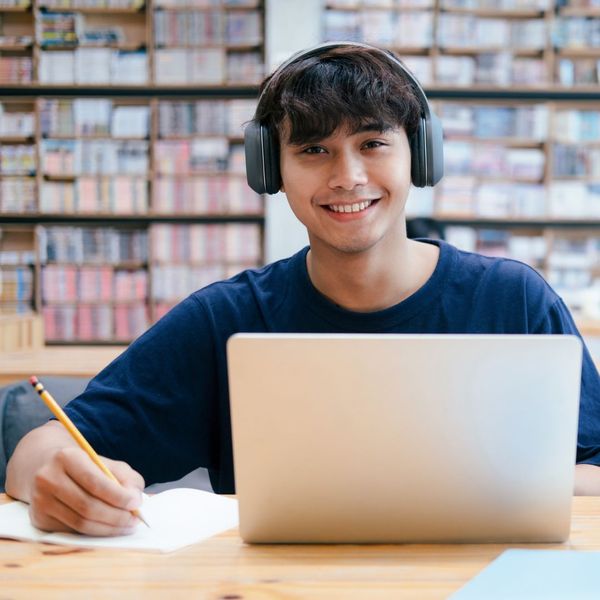 Male college student at library taking notes from laptop