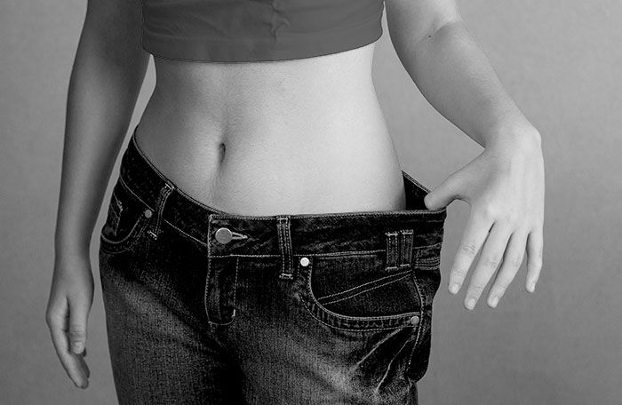 woman holding out waist of her jeans that are too big