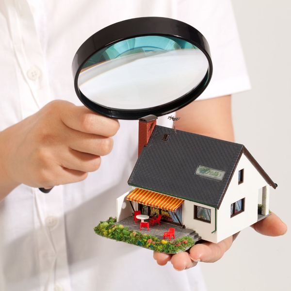 Person holding a house model and putting a magnifying glass up against it.
