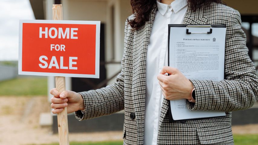 person holding home for sale sign