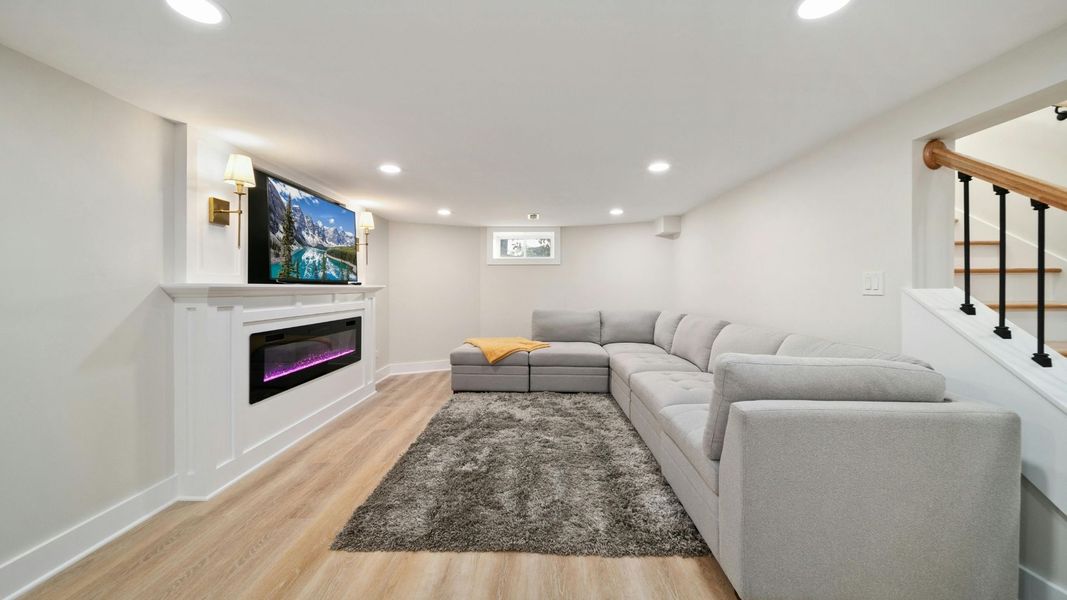 A finished basement with hardwood floors, a built in fireplace, and a comfortable couch