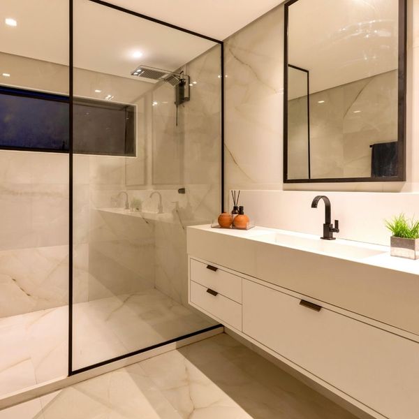 A bathroom with granite floors and walls, a long white modern sink, and black fixtures