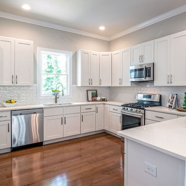 A kitchen with rich hardwood floors and white cabinets and countertops.